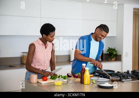 Cuisine de couple diversifiée sur l'îlot de cuisine, hacher la laitue et remuer la sauce dans une poêle Banque D'Images