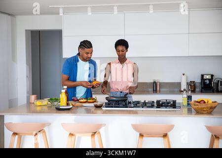 Couple diversifié cuisinant à l'île de comptoir dans la cuisine moderne hachant des légumes sur une planche à découper Banque D'Images