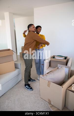 Couple diversifié embrassant dans le salon vide entouré de boîtes mobiles avec du papier bulle près du canapé Banque D'Images