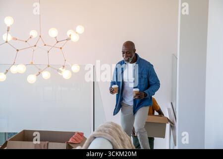 Divers amis déplaçant des boîtes sur l'escalier, homme afro-américain avec des tasses à café, espace de copie Banque D'Images