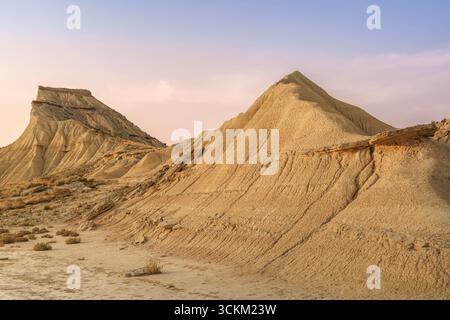 Formations argile érodées spectaculaires au coucher du soleil dans le désert de Bardenas Reales en Espagne. Badlands dorés, piliers de roche sédimentaire, paysage aride, montagnes du désert Banque D'Images