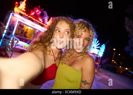 Deux jeunes femmes prenant un selfie la nuit dans un parc d'attractions Banque D'Images