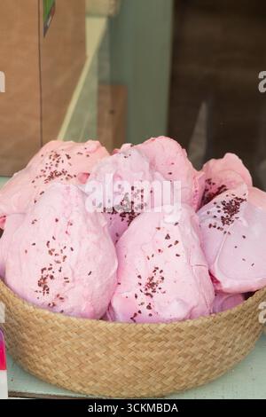 28 août 2025, Bruges, Belgique — Un panier en osier rempli de meringues rose pastel saupoudrées de flocons de chocolat. Banque D'Images