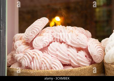 28 août 2025, Bruges, Belgique — Un panier rempli de tourbillons de guimauve rose pastel décorés de poussière de sucre. Banque D'Images