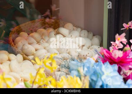 28 août 2025, Bruges, Belgique — Un panier rempli de petites meringues blanches rondes saupoudrées de graines de sésame, entouré de fleurs colorées dans un s. Banque D'Images
