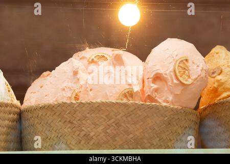 28 août 2025, Bruges, Belgique — grandes meringues roses décorées de tranches de citron séchées dans un panier sous un éclairage chaleureux. Banque D'Images
