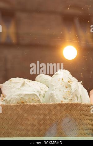 28 août 2025, Bruges, Belgique — panier de meringues vert pâle saupoudrées de miettes de sucre dorées exposées sous une lumière chaude. Banque D'Images
