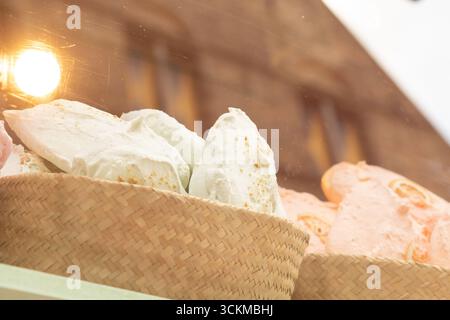 28 août 2025, Bruges, Belgique — Meringues blanches et vertes exposées ensemble dans un panier en osier sous une lumière chaude. Banque D'Images