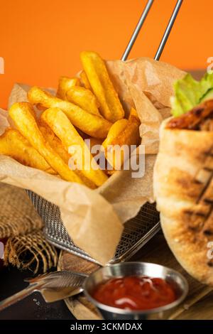 Frites dorées croustillantes dans un panier en papier sur une table sombre, gros plan avec un éclairage chaud Banque D'Images