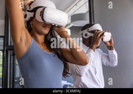 Divers collègues ajustant les casques vr blancs dans le bureau avec des conduits de plafond, des cloisons en verre Banque D'Images