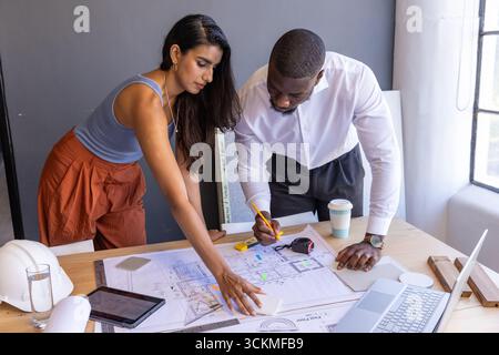 Divers collègues se penchant sur des plans dans le bureau de studio de design avec ordinateur portable, casque Banque D'Images