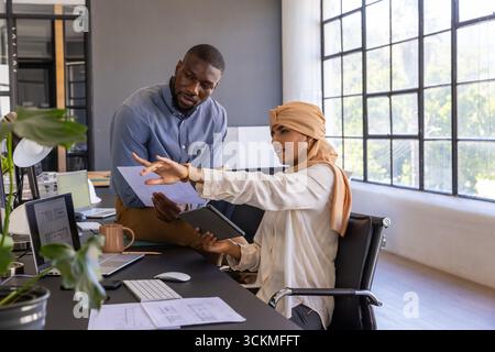 Divers collègues examinant les plans imprimés au bureau dans un espace ouvert portant une tenue professionnelle Banque D'Images