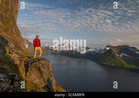 Randonneur sur Segla Peak, Senja, Norvège. Une vue spectaculaire d'un randonneur debout sur une paroi rocheuse surplombant le fjord profond et les montagnes environnantes Banque D'Images