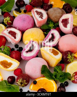Crème glacée mochi assortie colorée avec des baies fraîches, des agrumes et de la menthe sur fond blanc Banque D'Images
