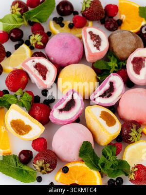 Crème glacée mochi assortie colorée avec des baies fraîches, des agrumes et de la menthe sur fond blanc Banque D'Images