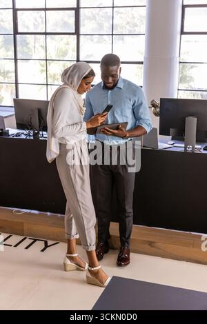 Divers collègues debout au bureau avec des moniteurs tenant smartphone et tablette Banque D'Images