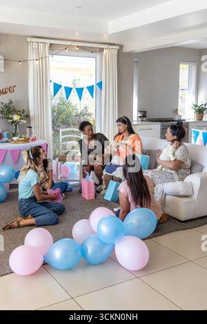 Diverses amies féminines assis autour des bébés sur le canapé avec des ballons, sacs-cadeaux dans le salon Banque D'Images
