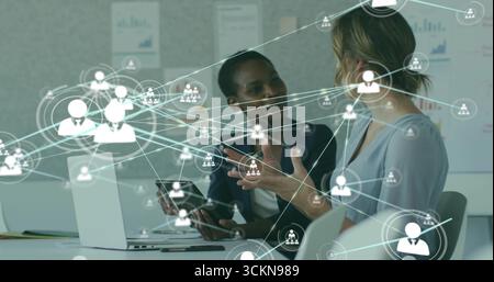 Deux femmes d'affaires dans Blazer collaborant à l'aide d'ordinateurs portables et de tablettes au bureau, avec superposition de réseau Banque D'Images