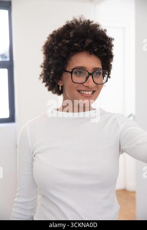 Femme afro-américaine prenant selfie dans le bureau à domicile portant des lunettes et chemise nervurée blanche Banque D'Images
