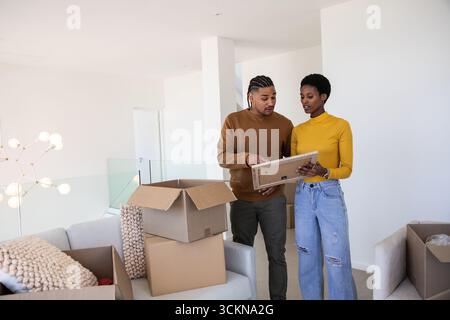 Couple diversifié tenant l'image encadrée et déballant les boîtes mobiles par canapé gris clair dans le salon Banque D'Images