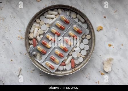 Diverses pilules et capsules médicales dans un bol en métal sur une table sale Banque D'Images