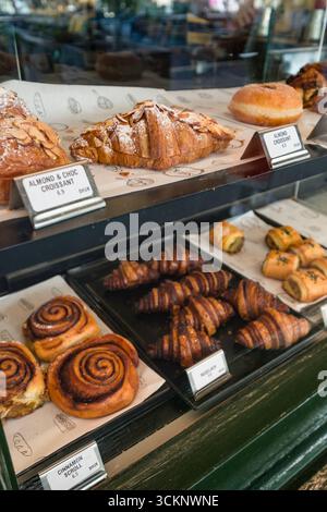Un délicieux assortiment de pâtisseries et de produits de boulangerie, y compris des croissants et des petits pains à la cannelle, présentés dans une vitrine de boulangerie. Une alléchante et v Banque D'Images