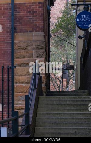 Une ruelle urbaine pittoresque avec des escaliers, encadrée par des murs de briques, menant à un fond paisible avec des arbres et un restaurant, The Rocks, Sydney Banque D'Images