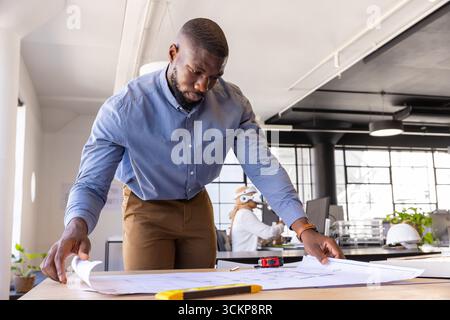 Divers collègues se penchant sur des plans de travail examinant des plans dans des bureaux ouverts, ruban à mesurer Banque D'Images