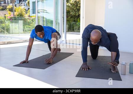 Père et fils afro-américains pratiquant des fentes de yoga sur une terrasse carrelée avec des tapis noirs Banque D'Images