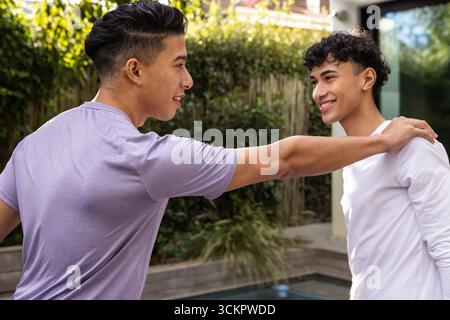 Divers amis masculins debout près de la terrasse de la piscine dans le patio de l'arrière-cour, bavardant à côté de la clôture de bambou Banque D'Images