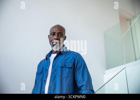 Homme aîné afro-américain debout près de la rampe de verre à l'escalier en chemise en denim sur t-shirt Banque D'Images
