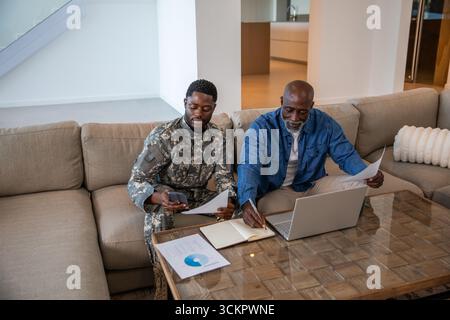 Père et fils afro-américains portant un uniforme camouflage examinant des rapports sur une table basse à la maison Banque D'Images