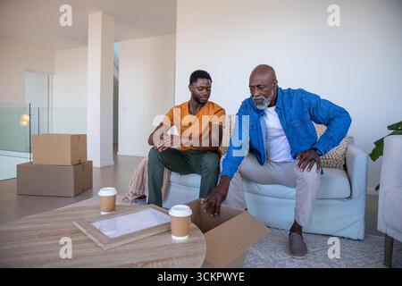 Père afro-américain et fils déballant des boîtes en carton sur le canapé dans le nouveau salon Banque D'Images