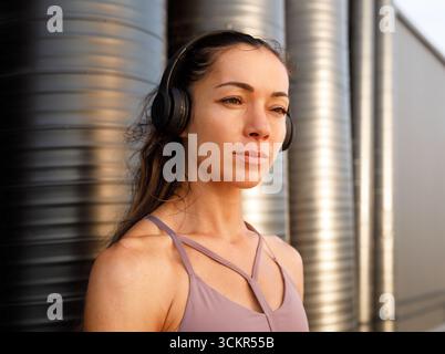 Portrait détaillé d'une jeune femme portant un casque sans fil debout à l'extérieur au coucher du soleil Banque D'Images