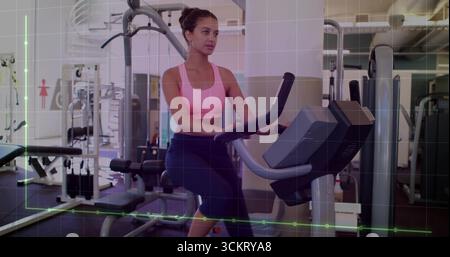 Femme pédalant portant un soutien-gorge rose et des leggings saisissant guidon sur vélo dans la salle de gym, avec haltères Banque D'Images