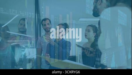 Pointez l'analyste tenant le marqueur en faisant des gestes vers les graphiques sur le mur de verre du bureau, avec l'équipe Banque D'Images