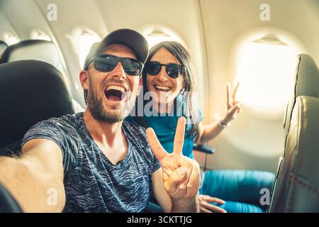 Couple souriant prenant selfie à l'intérieur de l'avion pendant le vol, montrant la joie, la liberté et le concept de style de vie de voyage Banque D'Images