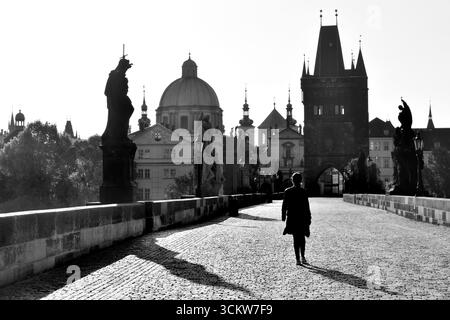Silhouette de jeune femme marchant sur l'emblématique pont Charles au lever du soleil dans la ville historique de Prague en noir et blanc Banque D'Images