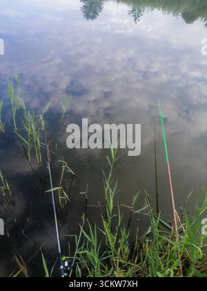 cannes à pêche sur fond d'eau d'étang calme. concept de pêche tranquille. Les nuages mous se déplacent au-dessus de la rivière calme Réflexion miroirs bleu ciel et blanc CLO Banque D'Images