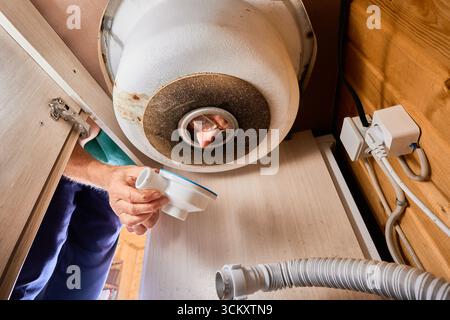 Installation de drain d'évier de cuisine, plombier regarde la pièce arrière en plastique à travers le trou de drainage dans l'évier de cuisine. Banque D'Images