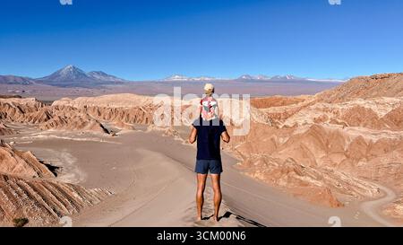 Homme touristique méconnaissable tenant son fils ou son enfant en bas âge sur les épaules, tout en se tenant debout sur le sommet de la dune et en regardant le volcan Licancabur. Banque D'Images
