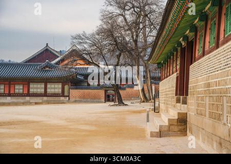 Vue détaillée de la cour du palais de Gyeongbokgung à Séoul avec des toits de tuiles ornées, des murs en bois rouge et des motifs dancheong complexes. Banque D'Images