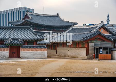 Vue détaillée de la cour du palais de Gyeongbokgung à Séoul avec des toits de tuiles ornées, des murs en bois rouge et des motifs dancheong complexes. Banque D'Images