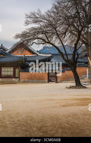 Vue détaillée de la cour du palais de Gyeongbokgung à Séoul avec des toits de tuiles ornées, des murs en bois rouge et des motifs dancheong complexes. Banque D'Images