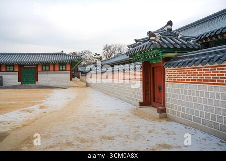 Vue détaillée de la cour du palais de Gyeongbokgung à Séoul avec des toits de tuiles ornées, des murs en bois rouge et des motifs dancheong complexes. Banque D'Images