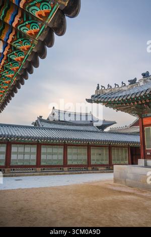Vue détaillée de la cour du palais de Gyeongbokgung à Séoul avec des toits de tuiles ornées, des murs en bois rouge et des motifs dancheong complexes. Banque D'Images