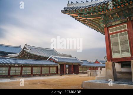 Vue détaillée de la cour du palais de Gyeongbokgung à Séoul avec des toits de tuiles ornées, des murs en bois rouge et des motifs dancheong complexes. Banque D'Images