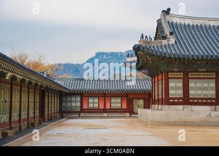 Vue détaillée de la cour du palais de Gyeongbokgung à Séoul avec des toits de tuiles ornées, des murs en bois rouge et des motifs dancheong complexes. Banque D'Images