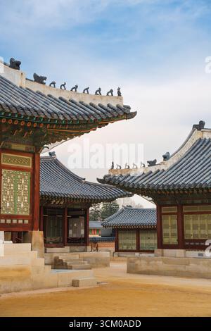 Vue détaillée de la cour du palais de Gyeongbokgung à Séoul avec des toits de tuiles ornées, des murs en bois rouge et des motifs dancheong complexes. Banque D'Images
