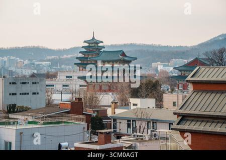 Vue surélevée de la pagode du Musée folklorique national de Corée avec son toit en tuiles bleues, s'élevant au-dessus des bâtiments urbains de Séoul et des collines lointaines. Banque D'Images